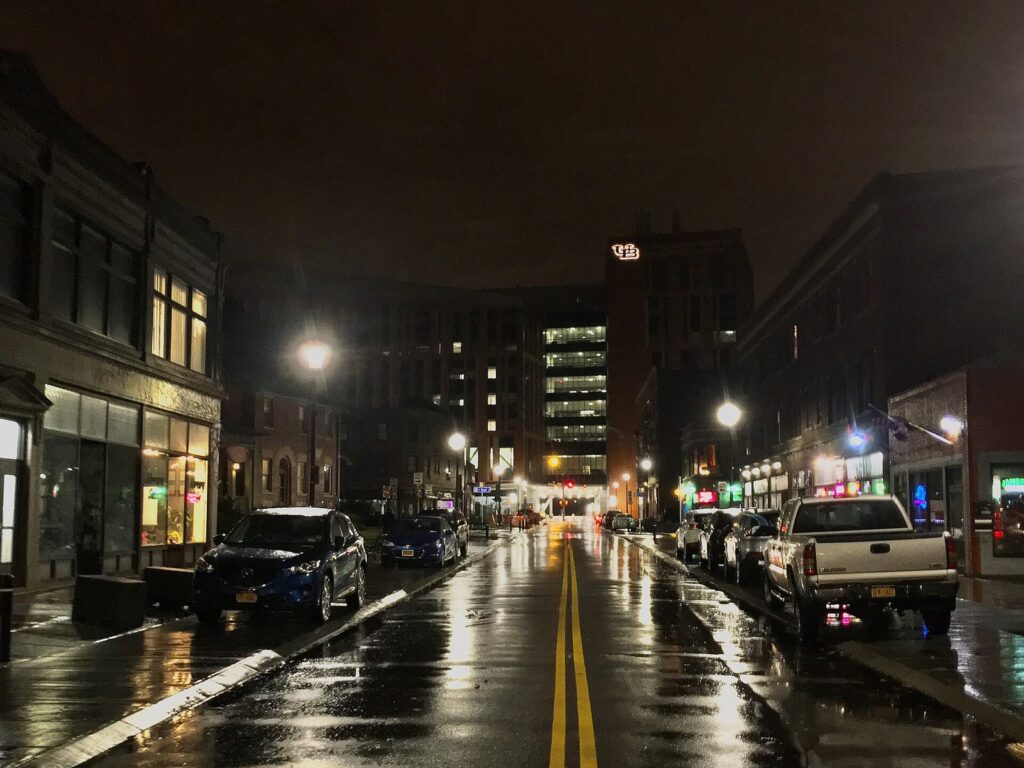 Allen Street in Buffalo's Allentown neighborhood at night, with lit bars and shopfronts reflected on the wet street