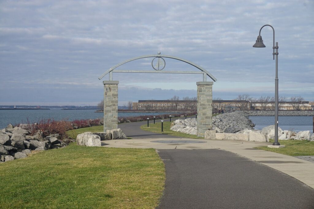 A paved lakeside path passing under a stone and steel arch at Buffalo Harbor State Park