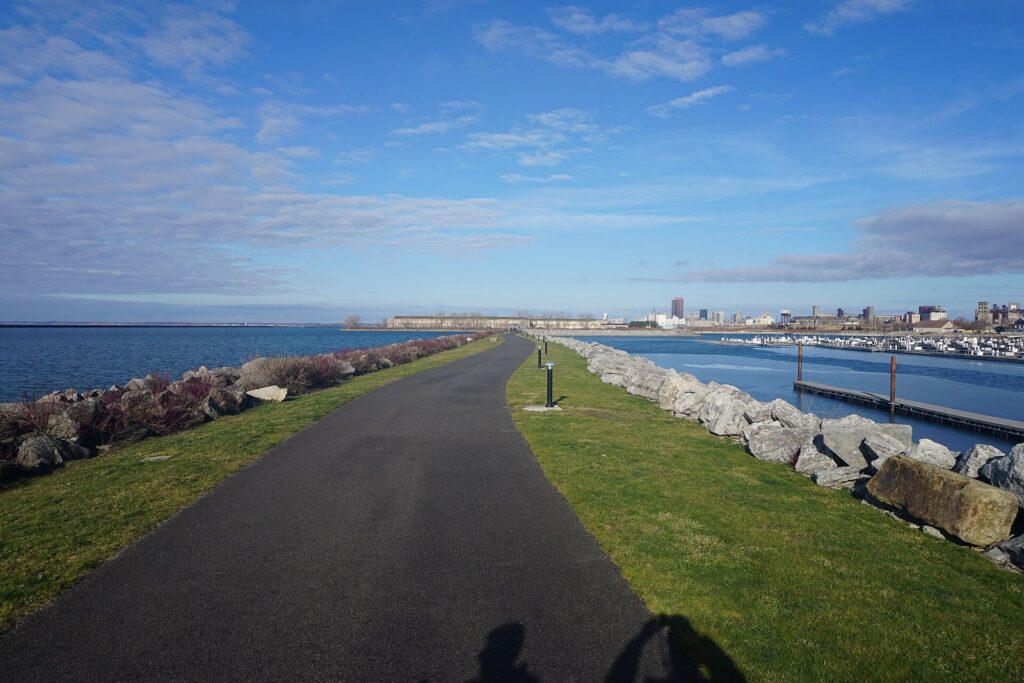 A paved path along the breakwater at Buffalo Harbor State Park, with the marina and downtown Buffalo in the distance