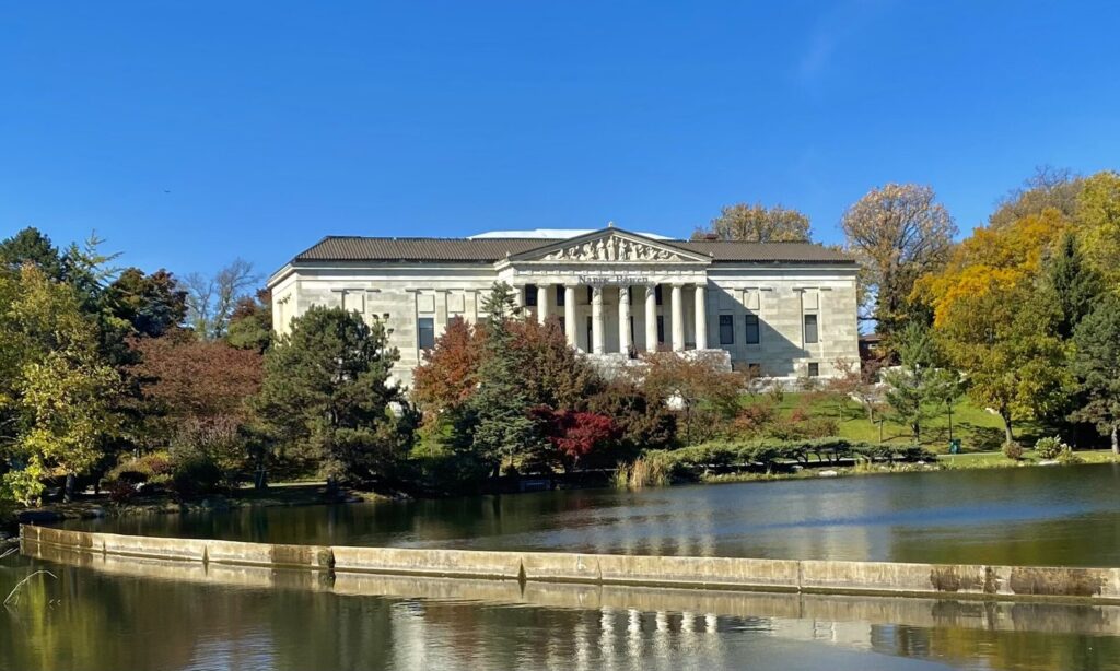 The Buffalo History Museum's marble portico above Mirror Lake and the Japanese Garden, framed by red and gold autumn trees