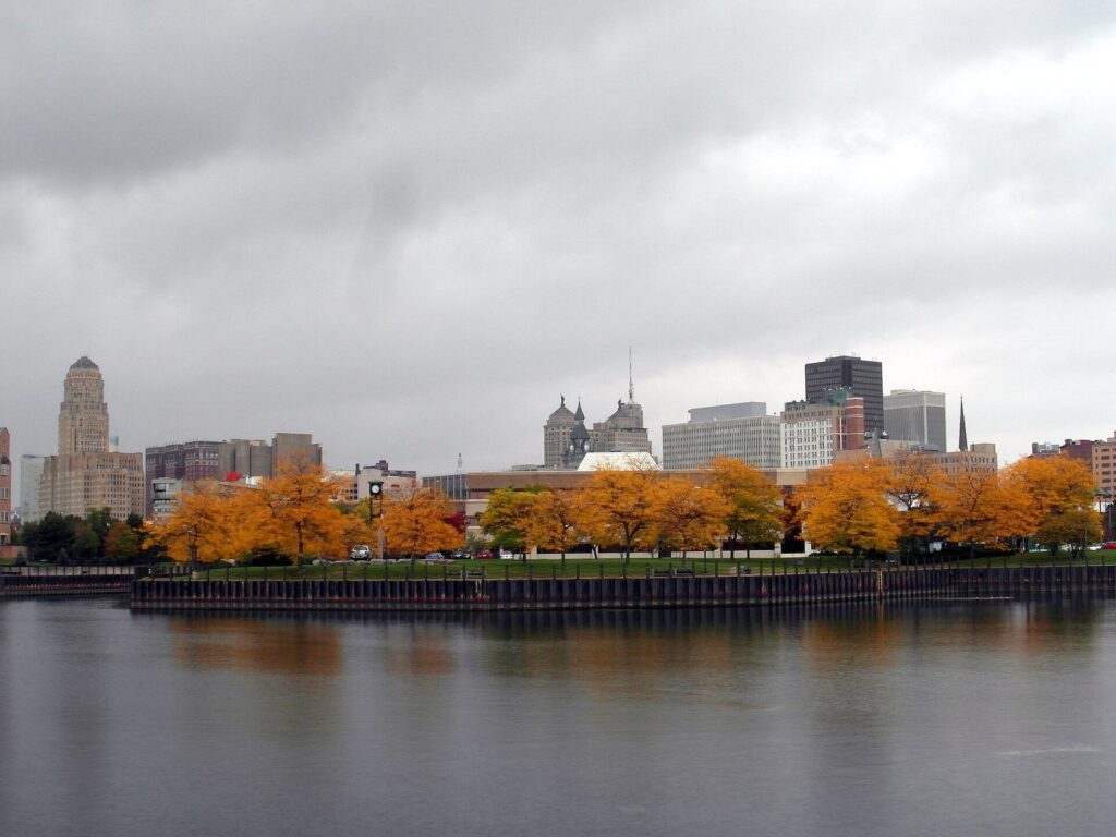 Downtown Buffalo's skyline and City Hall above a row of orange autumn trees, seen across the water from the Erie Basin Marina, the view that opens this Buffalo NY waterfront guide
