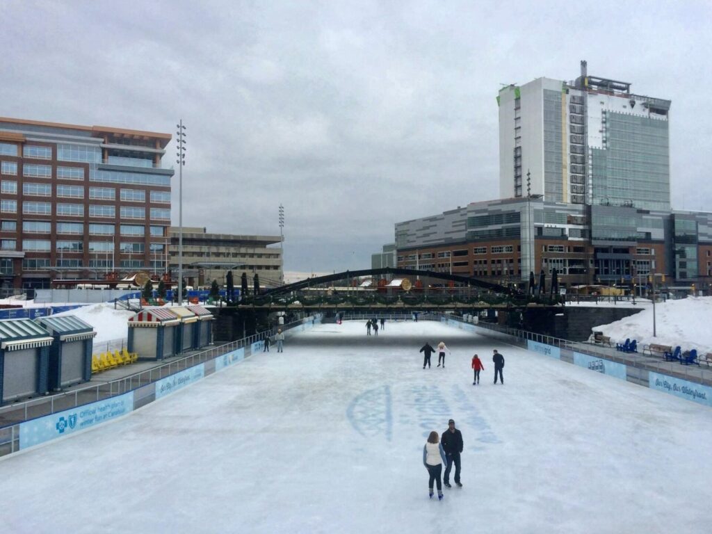 Skaters on the outdoor ice rink at Canalside in Buffalo in winter, with downtown buildings behind