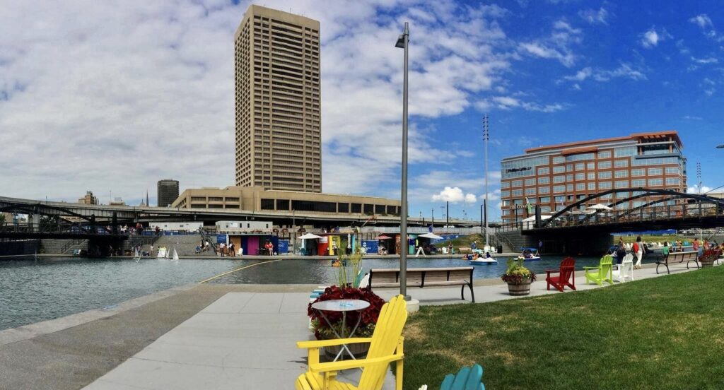 Colorful Adirondack chairs beside the canal at Canalside in Buffalo on a sunny late-summer day, with downtown towers behind