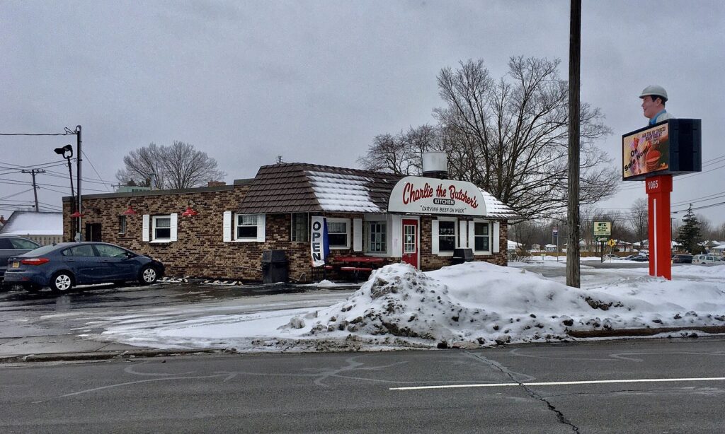 Charlie the Butcher's Kitchen, a small brick restaurant with a tall roadside sign, on a snowy winter day in Amherst