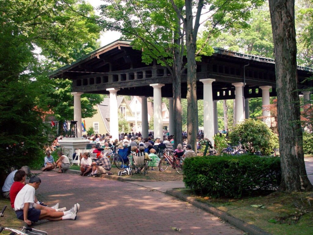 People gathered on benches and lawn chairs at the open-sided Hall of Philosophy at Chautauqua Institution in summer
