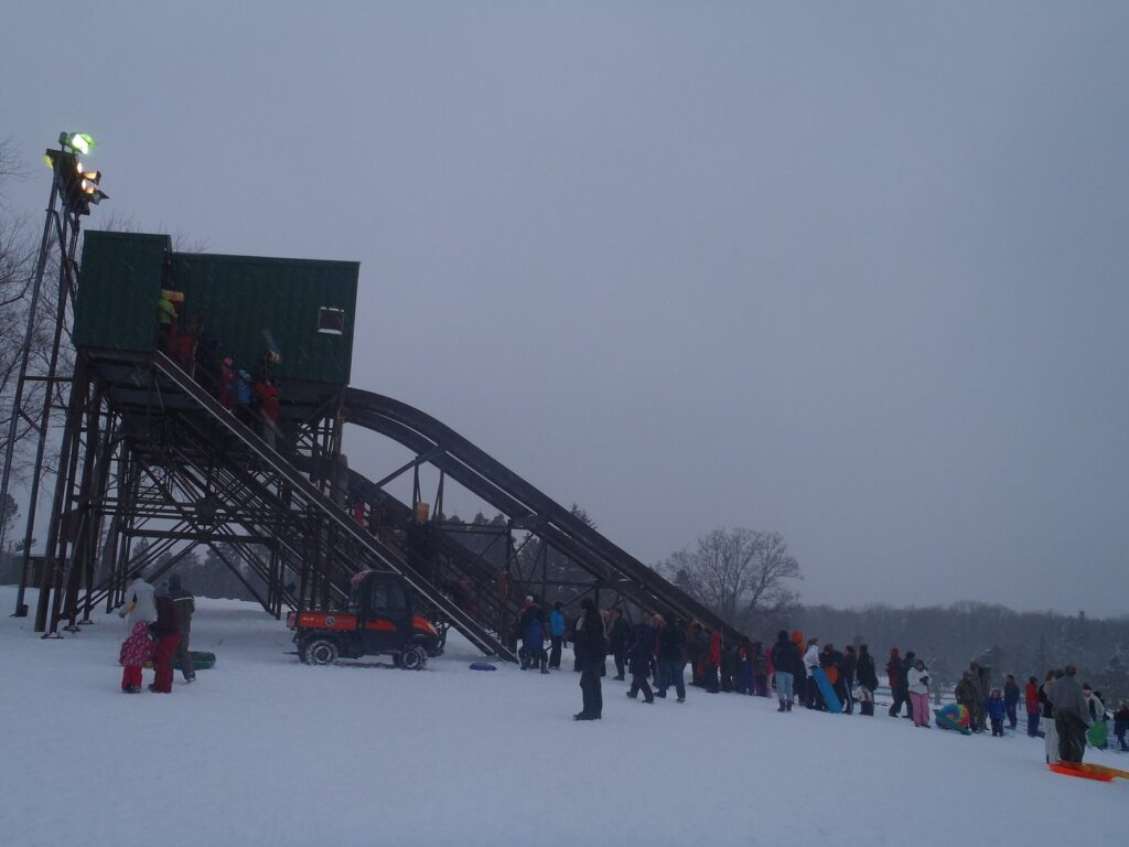 Families in snowsuits lining up at the wooden toboggan chutes at Chestnut Ridge Park near Buffalo on a snowy winter day