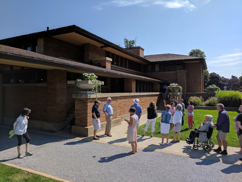 A tour group including a visitor in a wheelchair outside the entrance of Frank Lloyd Wright's Darwin D. Martin House
