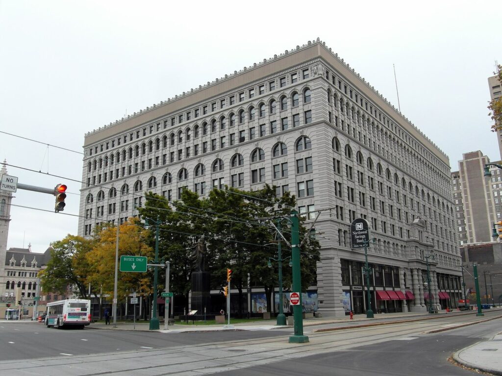 The gray Ellicott Square Building filling a downtown Buffalo block beside Main Street and the Metro Rail tracks