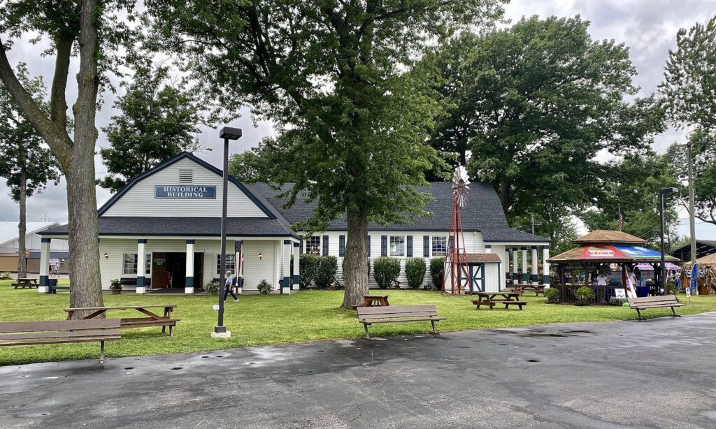 The white Historical Building and picnic tables under shade trees on the Erie County Fair grounds in Hamburg