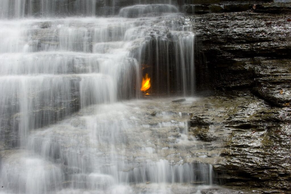 A natural gas flame burning behind a thin waterfall on layered shale at Eternal Flame Falls in Chestnut Ridge Park, south of Buffalo