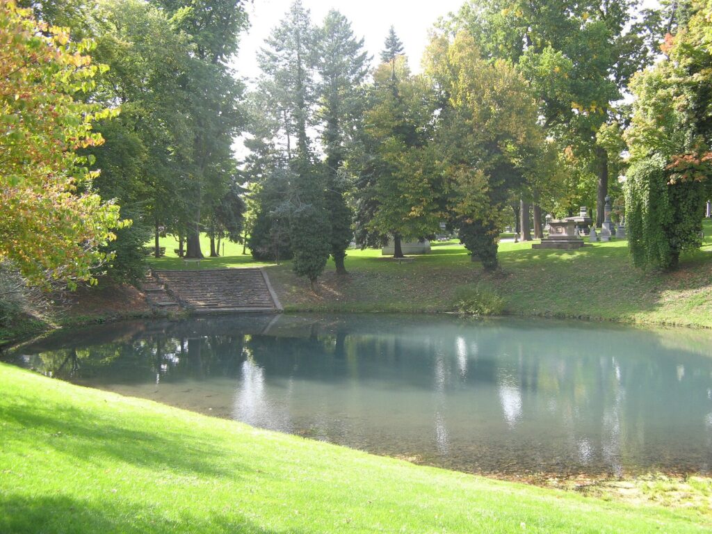 A still pond at Forest Lawn Cemetery in Buffalo framed by tall trees just starting to turn