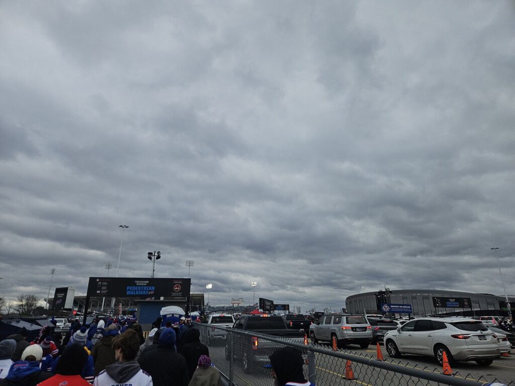 Fans walking toward the old Highmark Stadium under a gray sky, with the new Highmark Stadium visible across the road in November 2025
