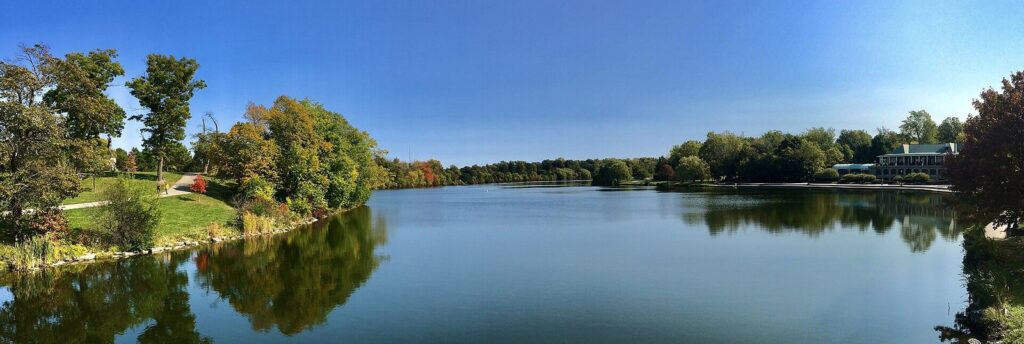 Panoramic view of Hoyt Lake in Delaware Park with early autumn color on the trees and blue sky reflected in the water