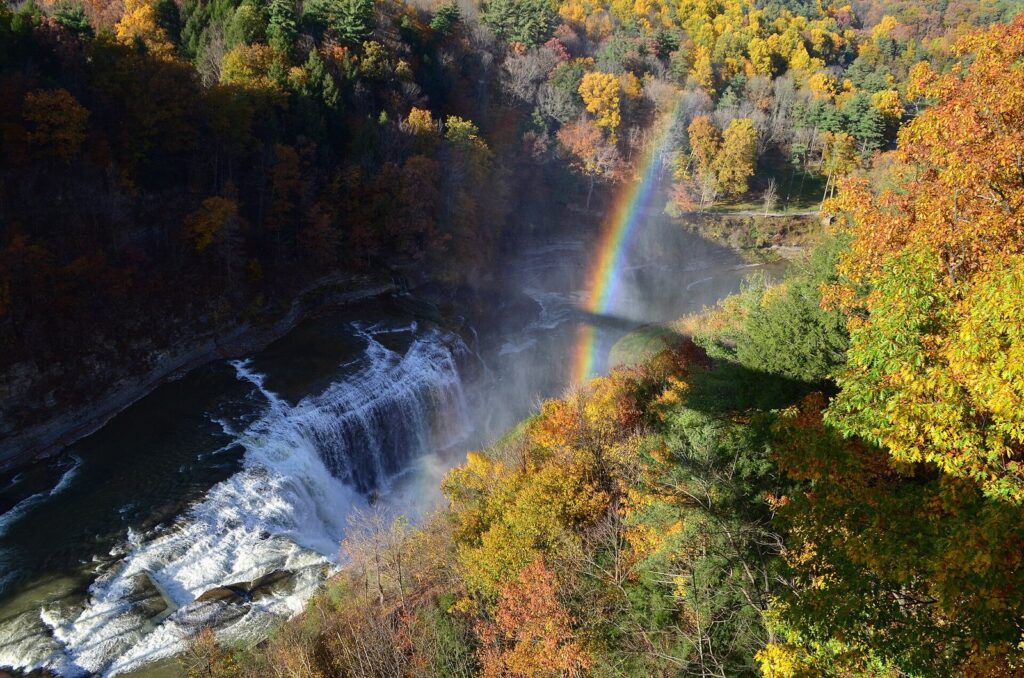Autumn color on the walls of the Letchworth gorge above a waterfall with a rainbow in its spray
