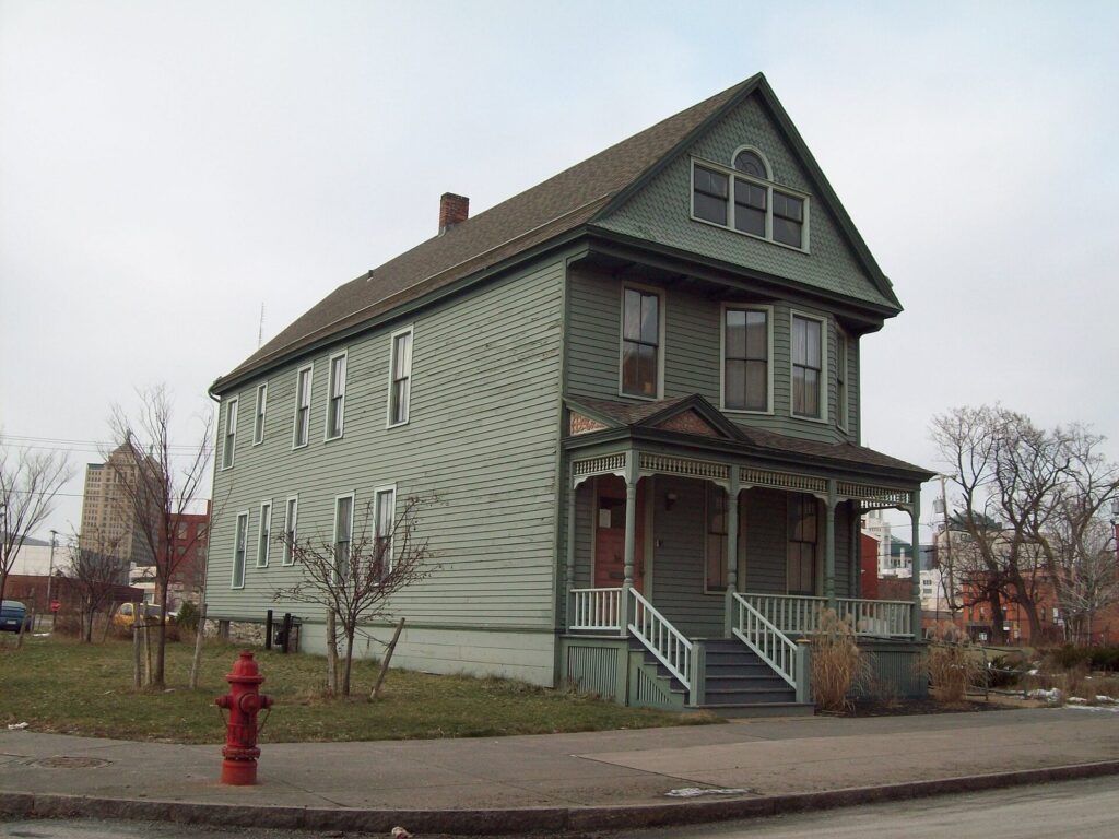 The two-story green clapboard Nash House Museum in Buffalo, with a porch and a fire hydrant out front