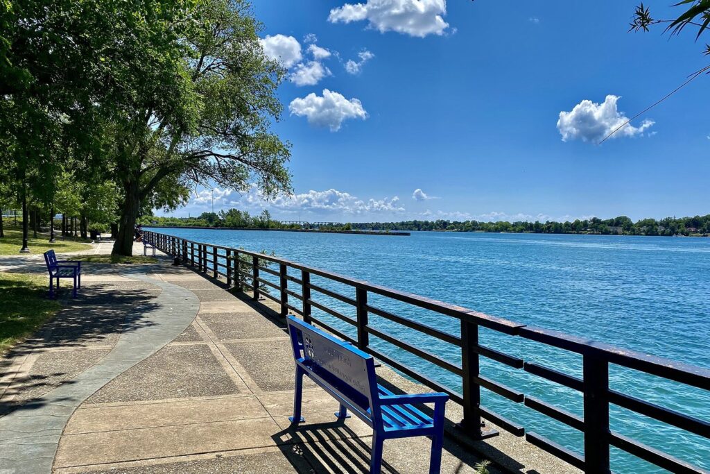 A riverside path with blue benches beside the Niagara River at Tow Path Park in Buffalo's Black Rock neighborhood