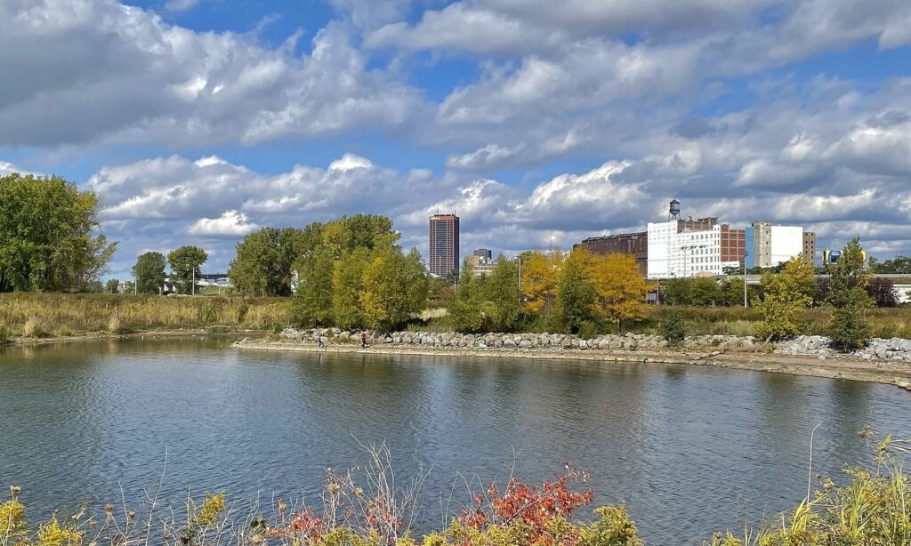 A calm inlet on Buffalo's Outer Harbor framed by autumn trees, with downtown buildings in the distance