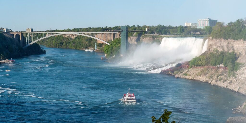 The Rainbow Bridge arching over the Niagara River below the American Falls, with a tour boat in the water