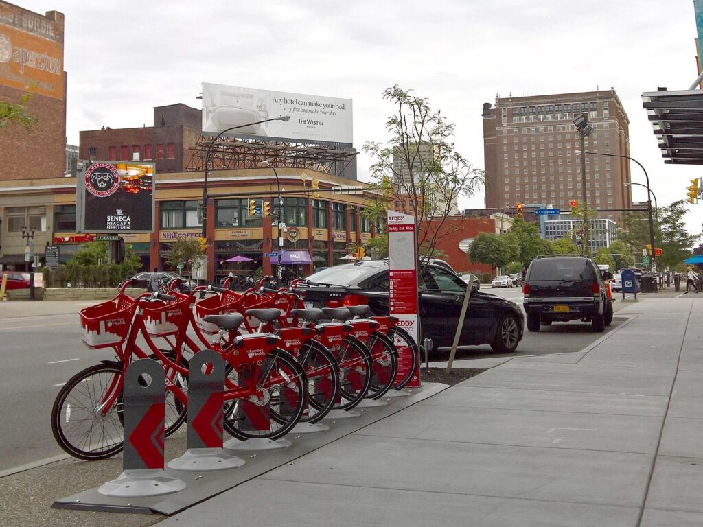 A row of red Reddy Bikeshare bicycles docked at a rack on a downtown Buffalo sidewalk