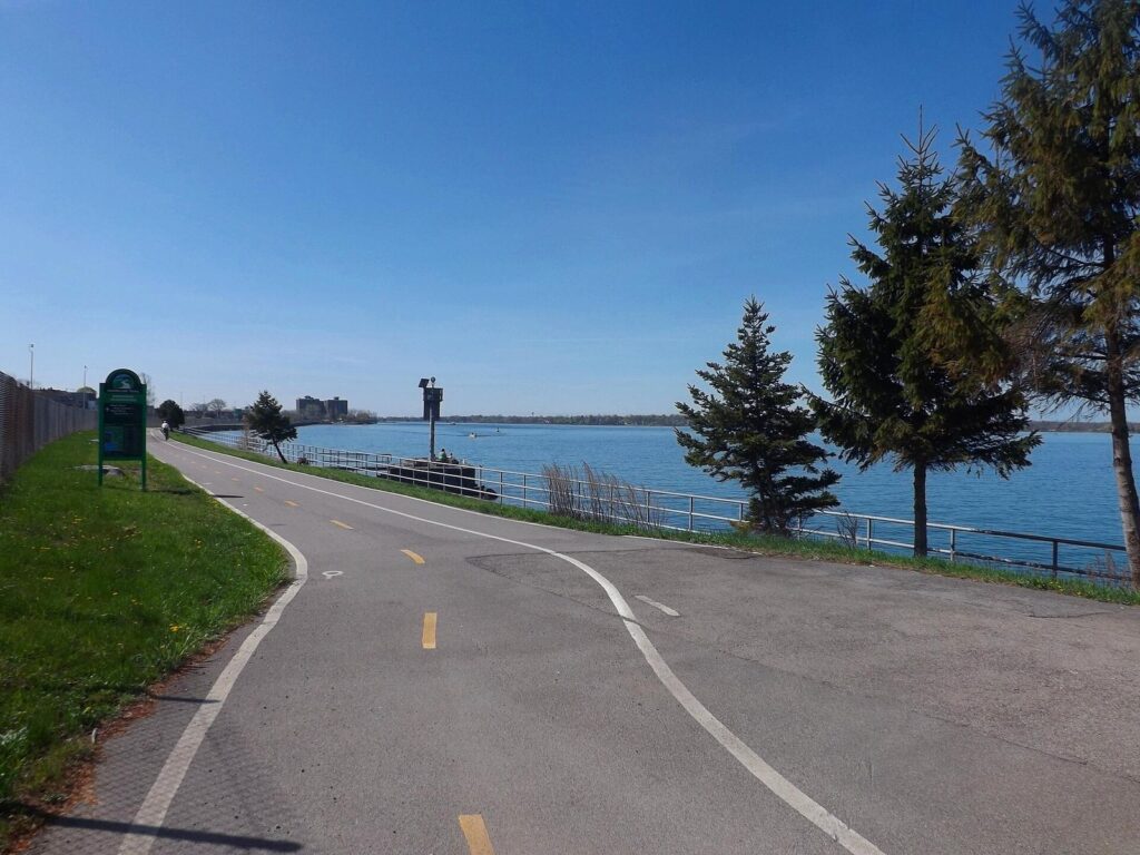 A paved multi-use path curving beside the Niagara River in Buffalo's Riverside Park under a blue sky